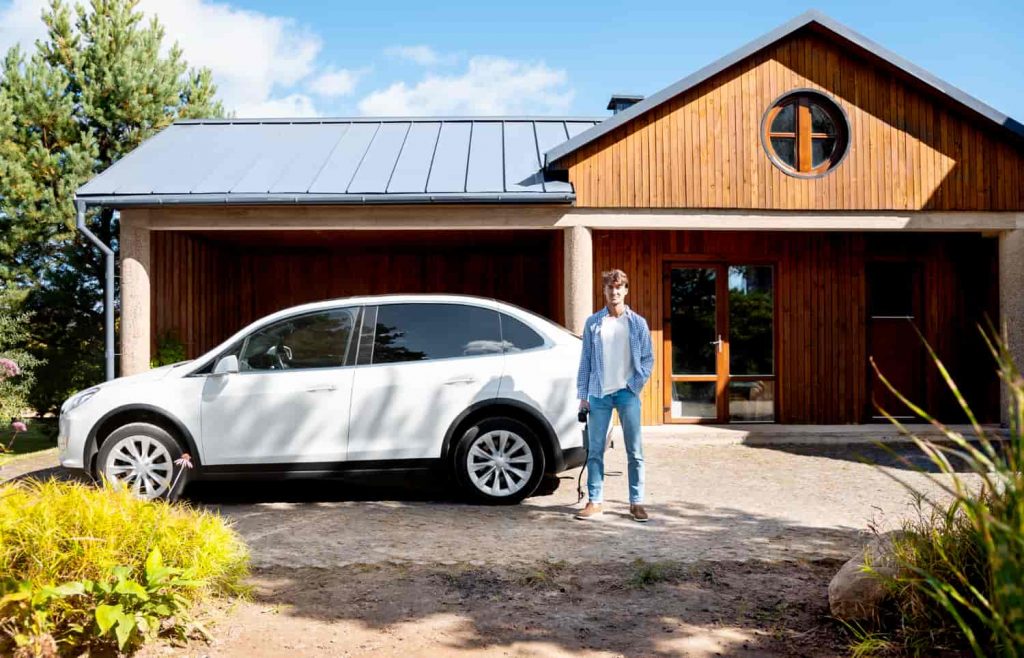 Persona posando frente a casa con punto de recarga solar para vehículos eléctricos